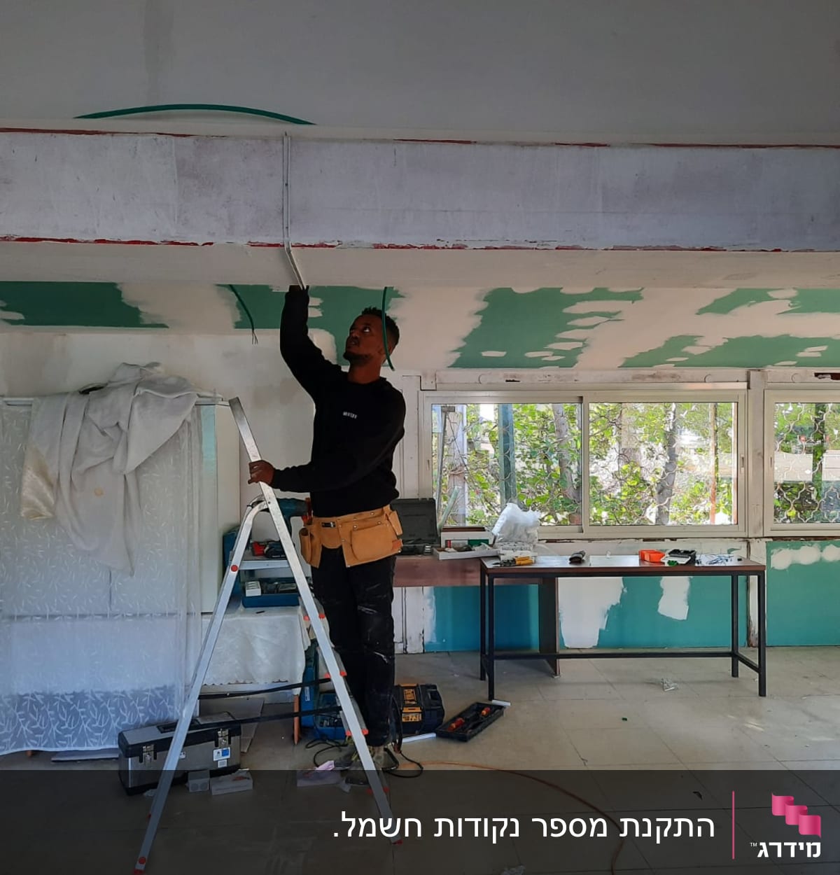 חשמלאי עובד על תקרה עם סולם וכלי עבודה